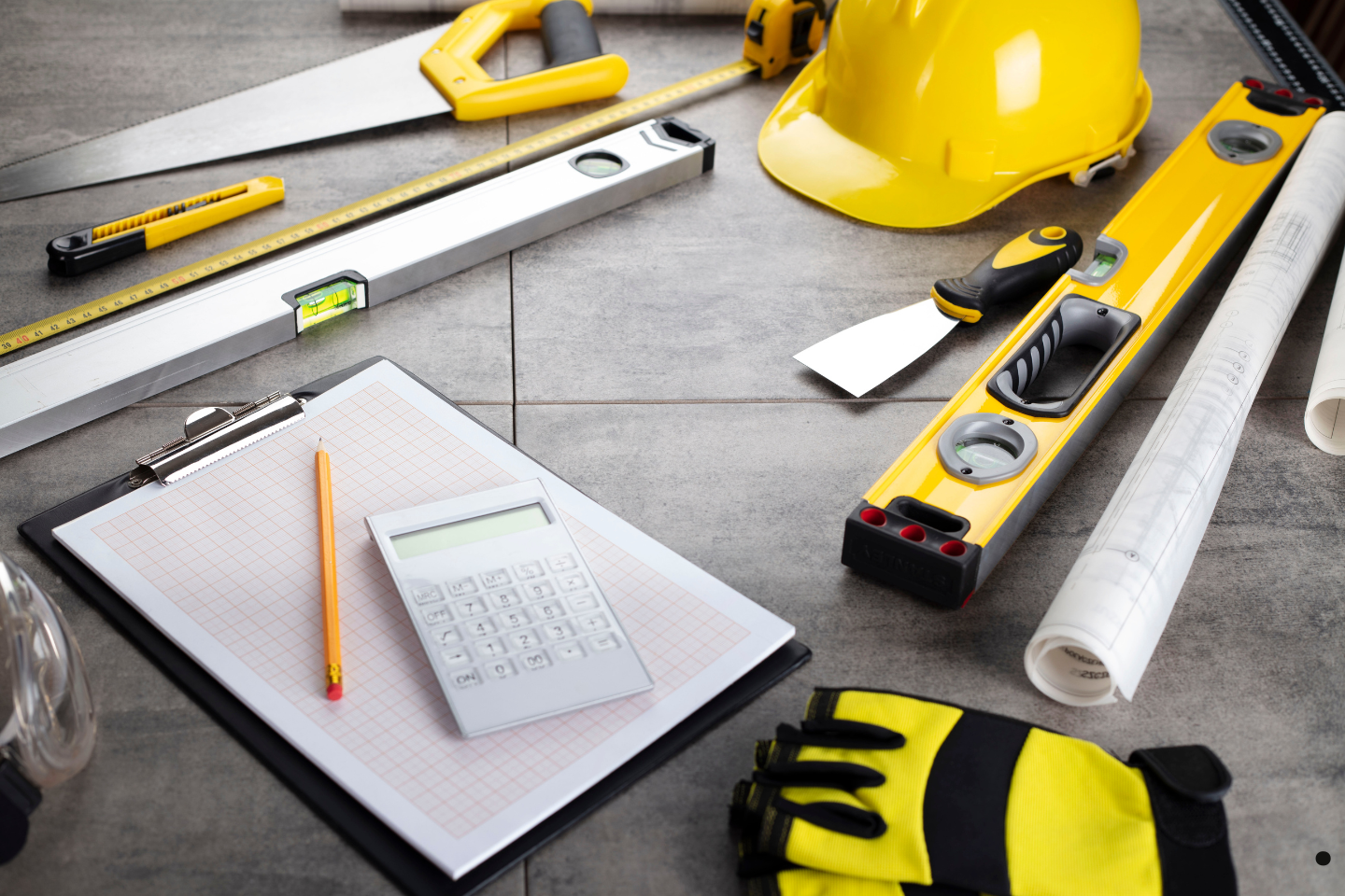 Construction tools, blueprints, a calculator, and safety gear arranged on a worktable.