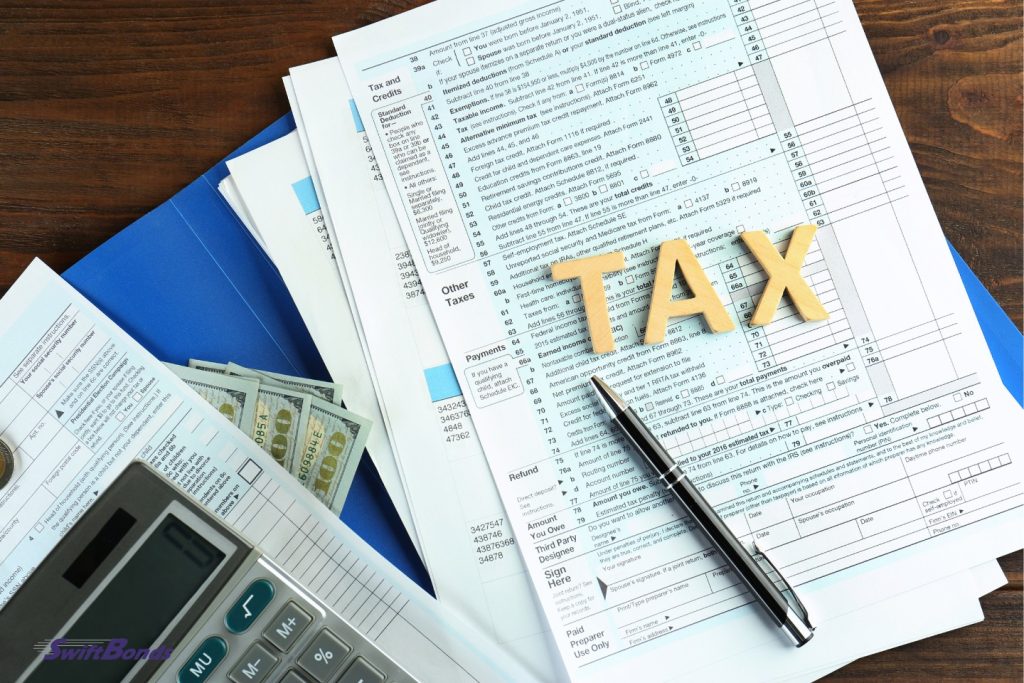 Word tax on a table with paperwork, dollar dollars, a pen, and a calculator.