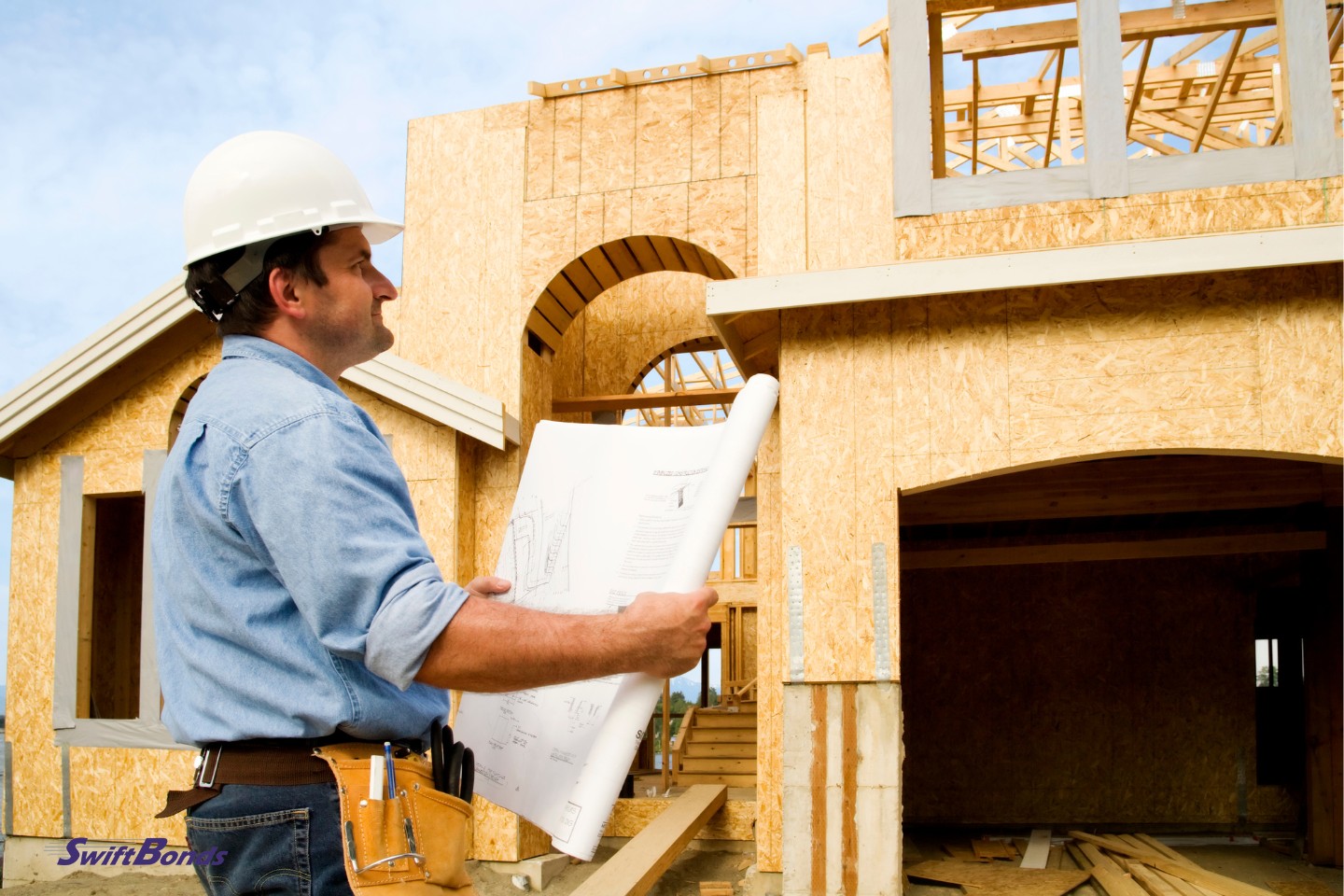 On the construction site, a worker is examining a set of building designs.