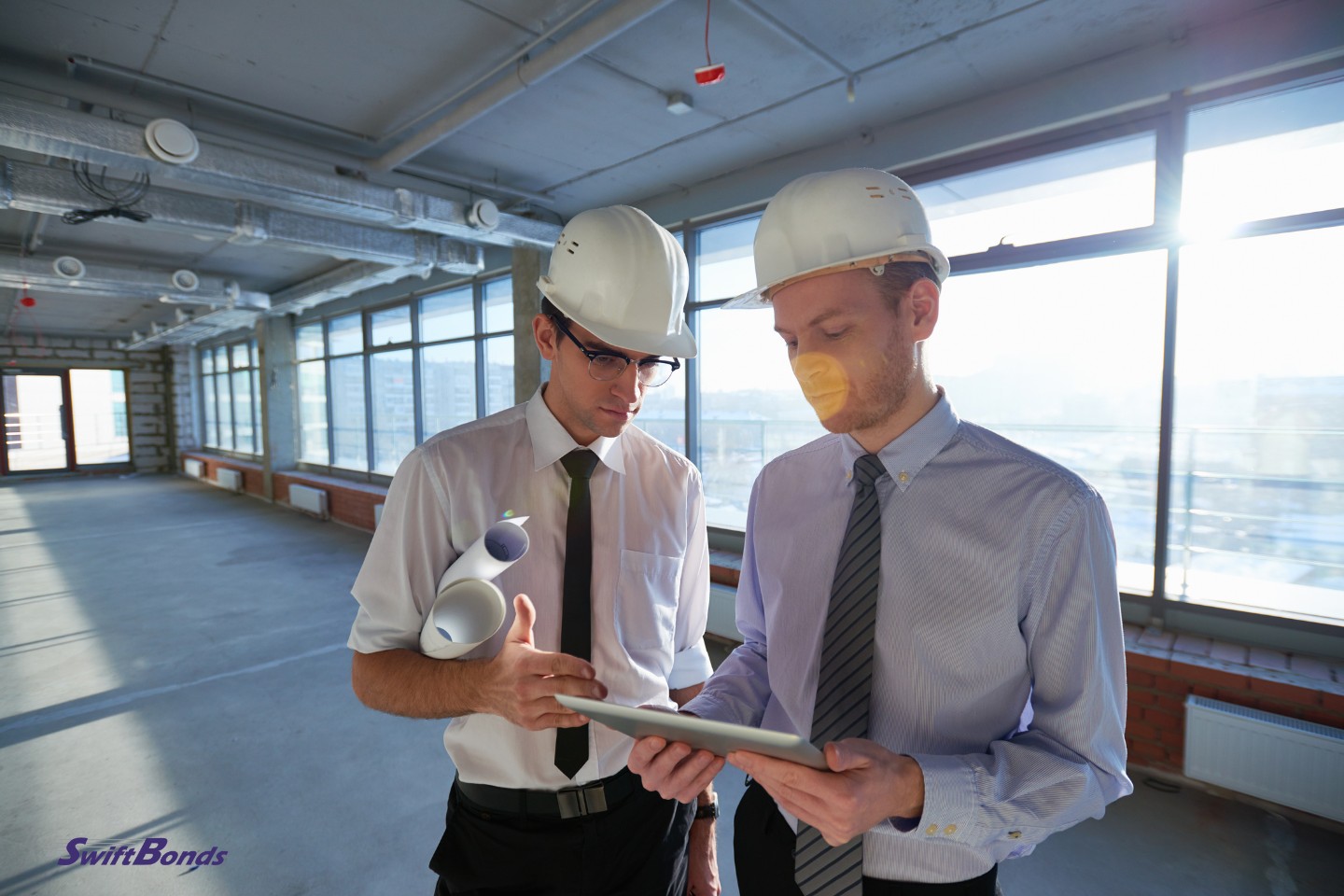 Inside the completed building, two hardhat-wearing construction workers are using a tablet computer to study the project.