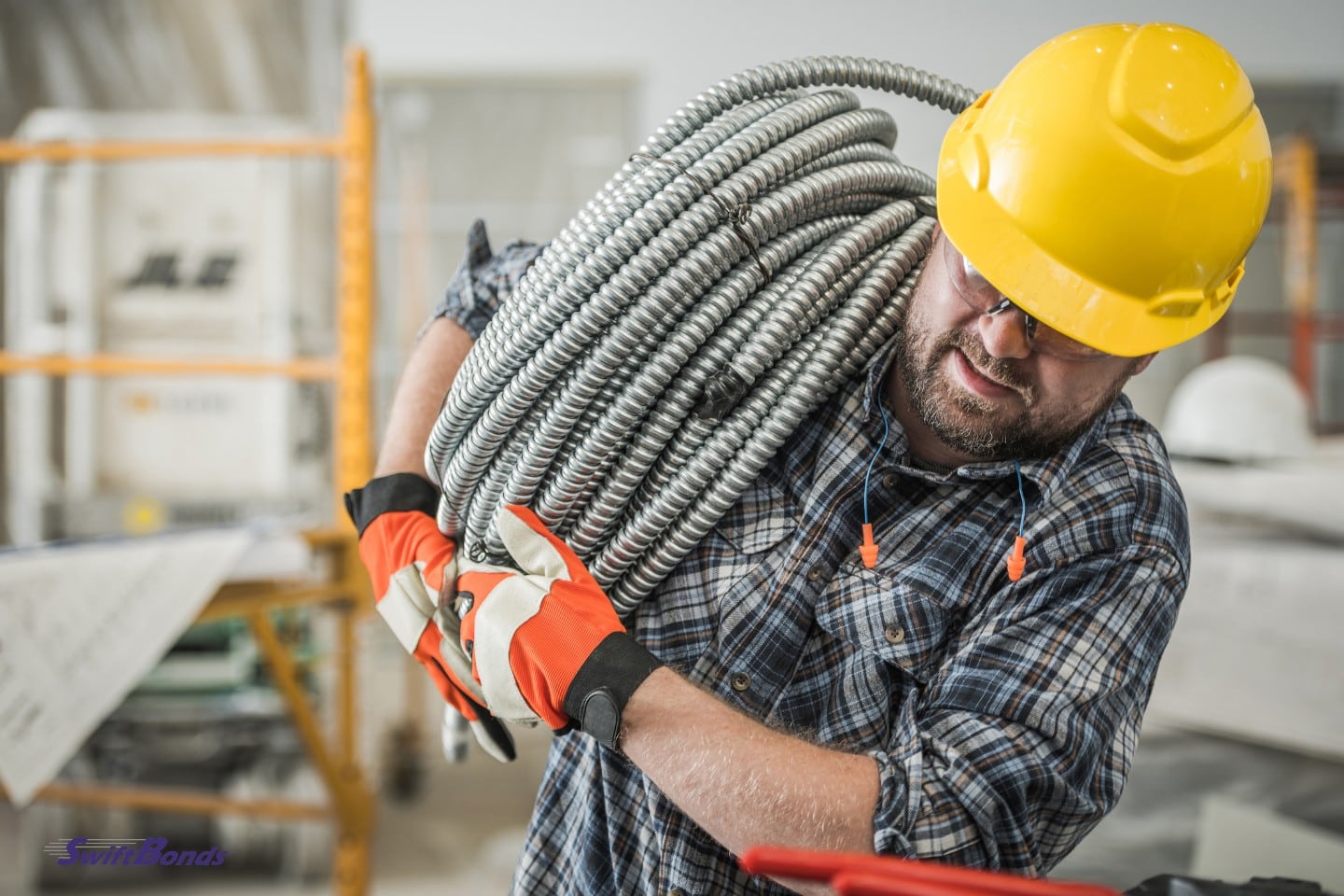Moving heavy metal power cables is being done by a contractor wearing a yellow safety helmet.