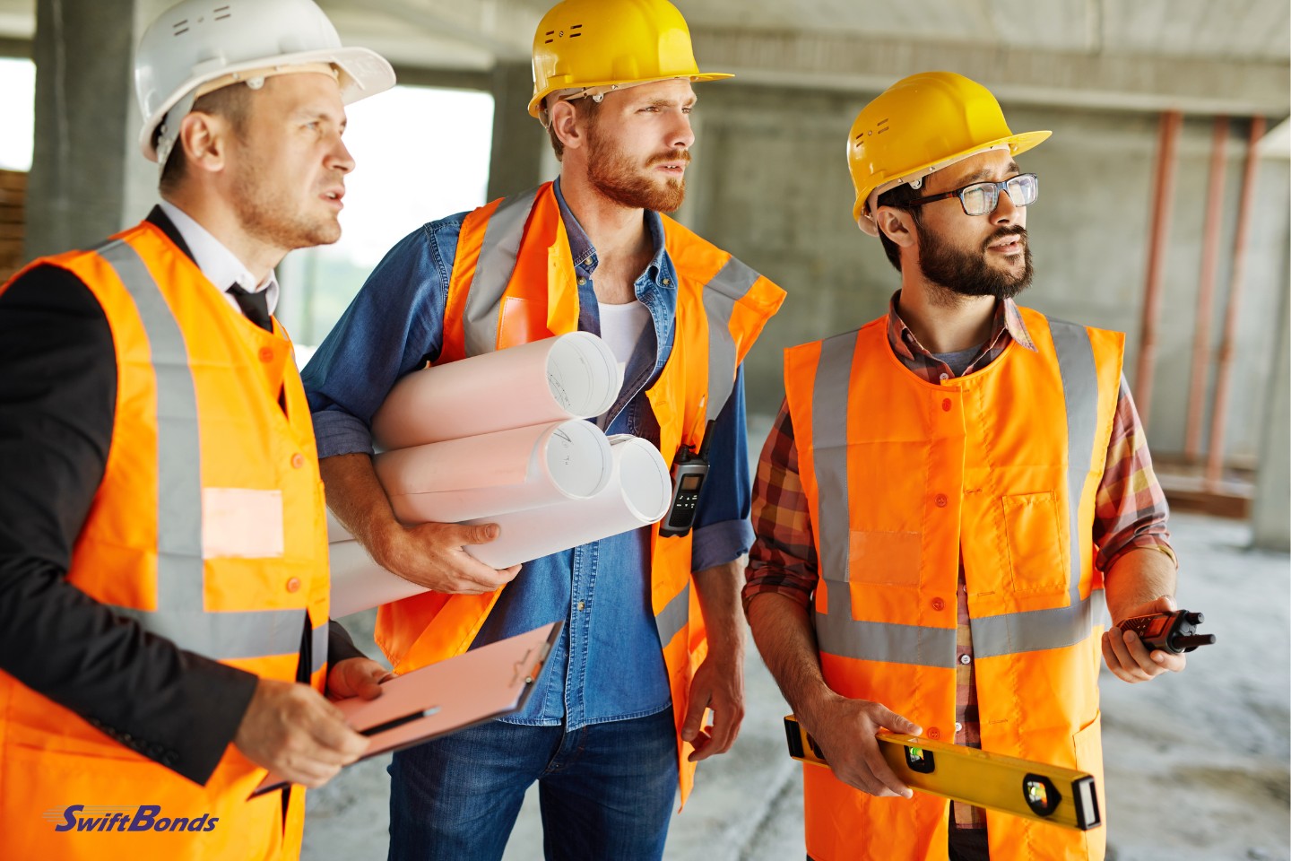 On a building site, three professionals wearing hardhats and uniforms stand.