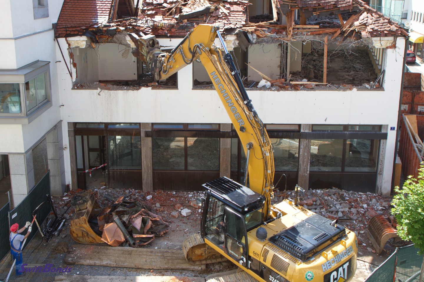 A wrecker building equipment and a blue-uniformed contractor are engaged in the demolition of the old house.