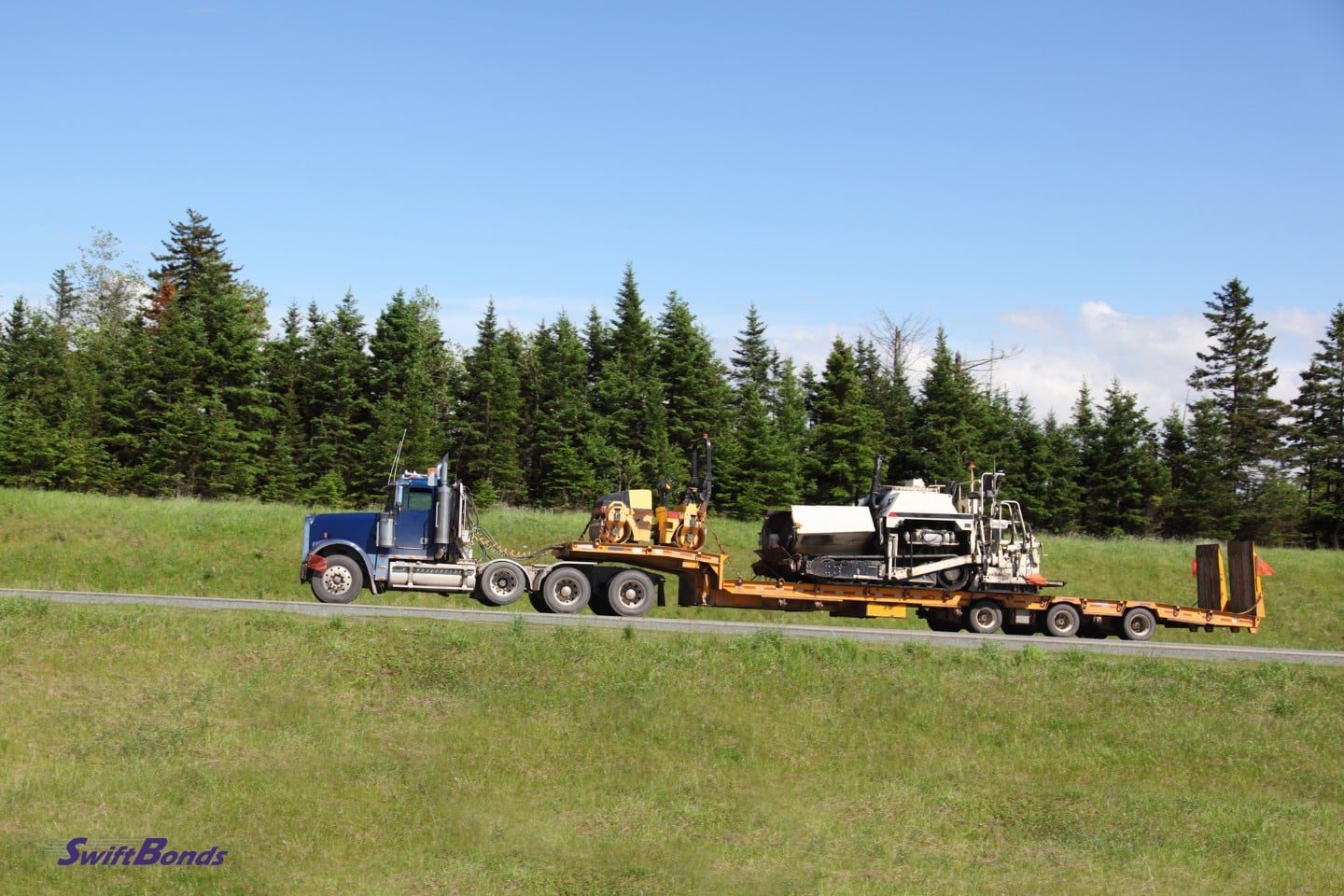 Heavy paving equipment being transported by semi-truck.