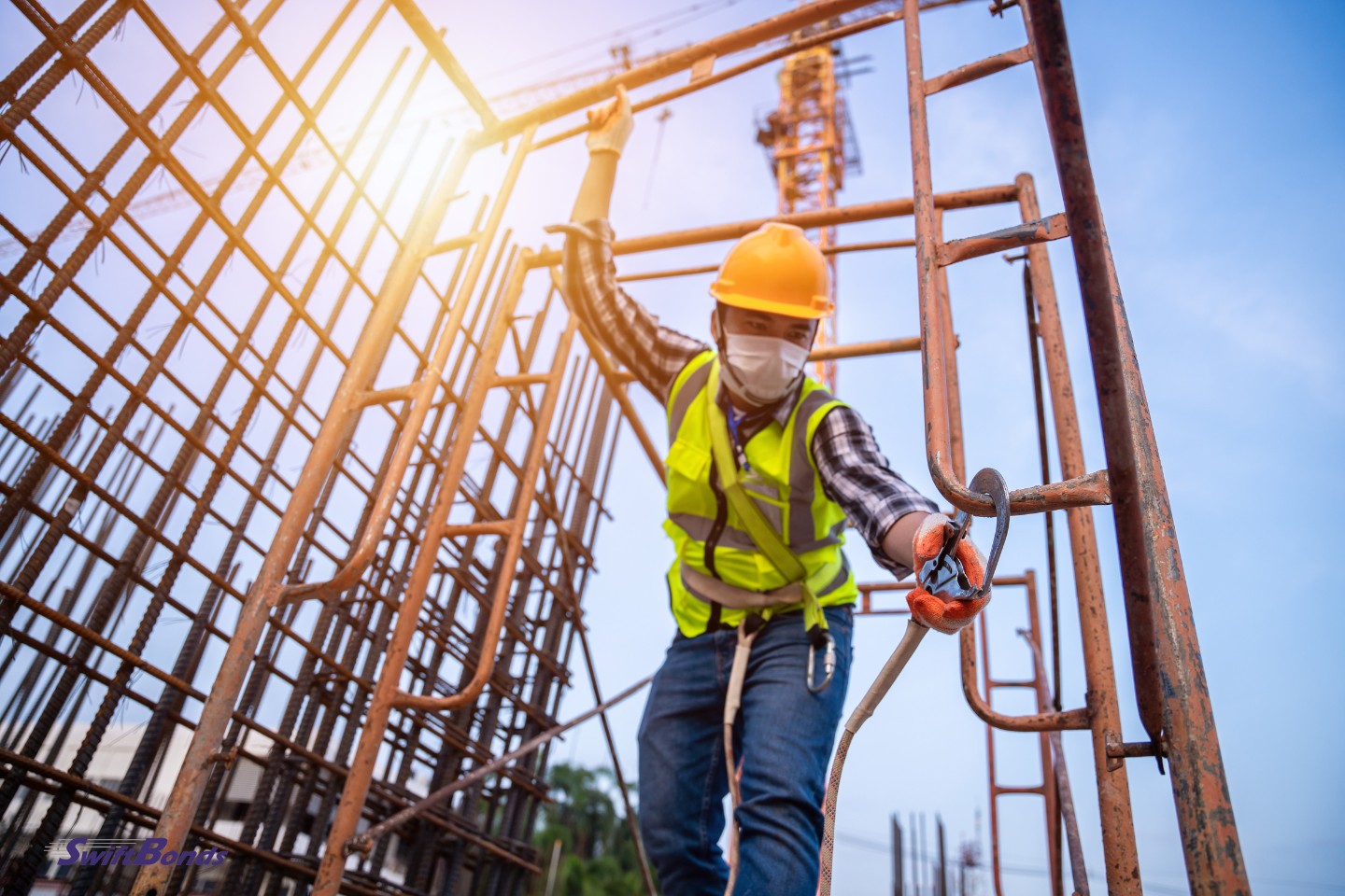 Asian contractor works at heights wearing a yellow hard hat and vest.