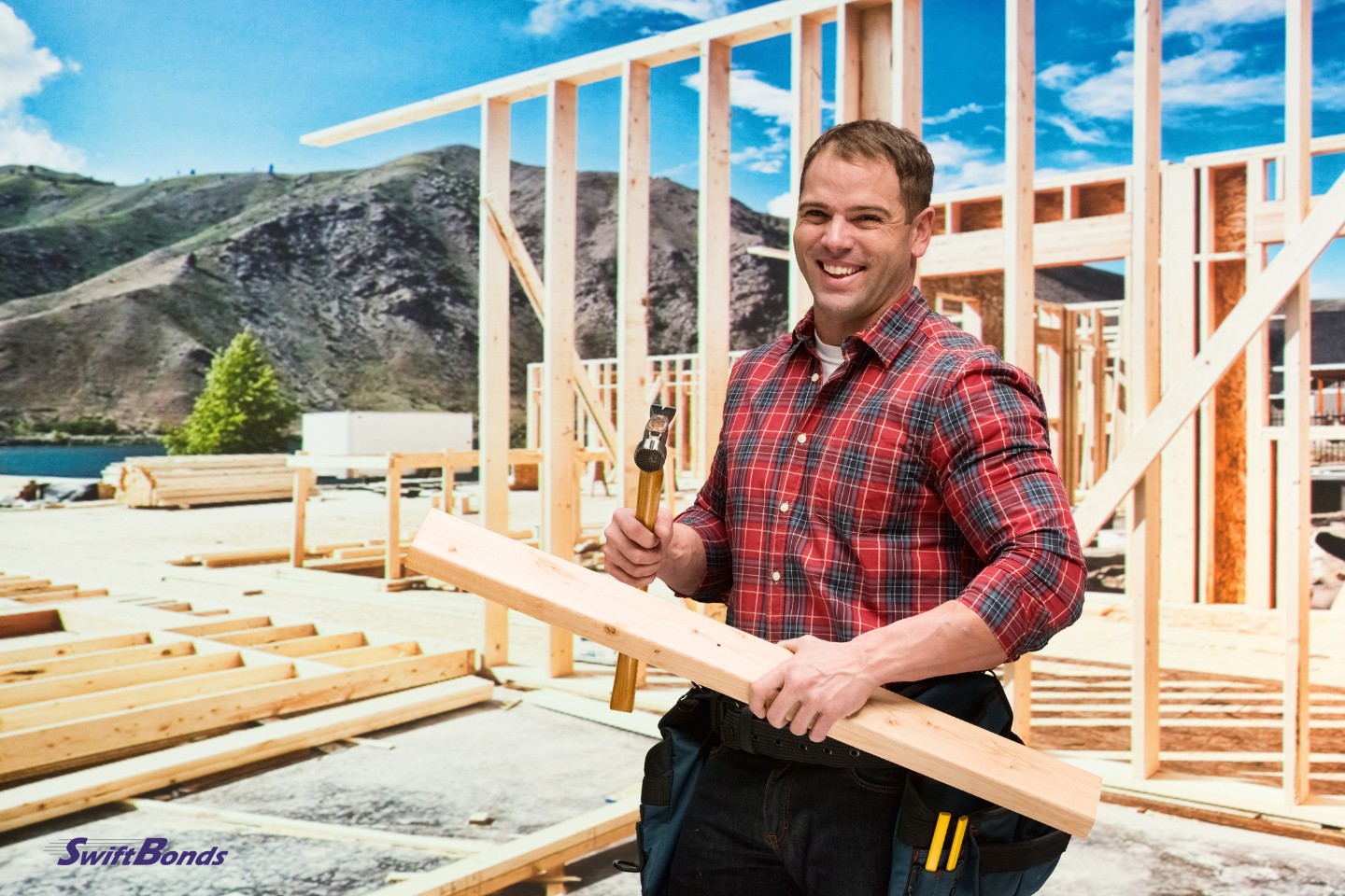 Building contractor grinning while working outside. holding a chunk of wood with a hammer.