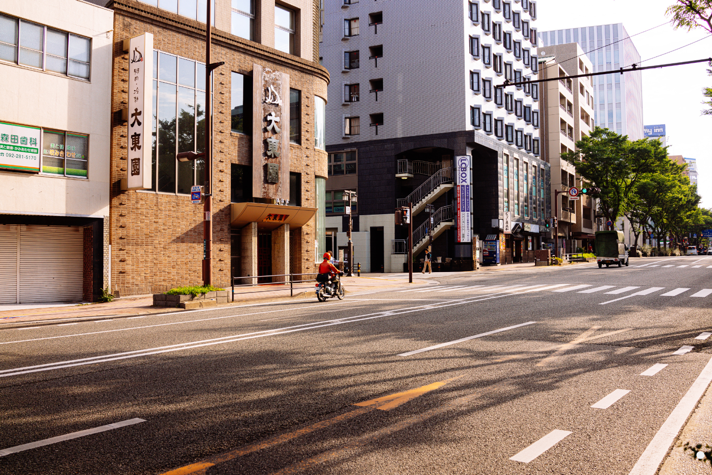 Quiet urban street with mixed-use buildings and a motorcyclist riding along the roadway.