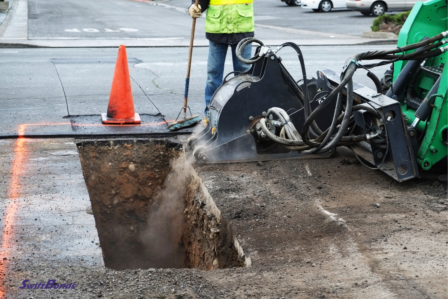 Open utility trench across city street while crew working on a rainy day.