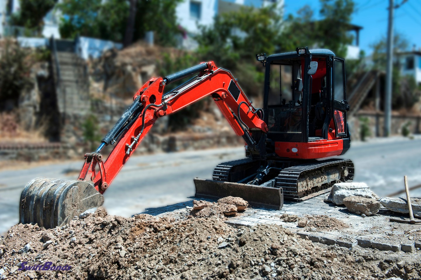 Cement road is being dug up and destroyed by a little excavator in the middle of the road.
