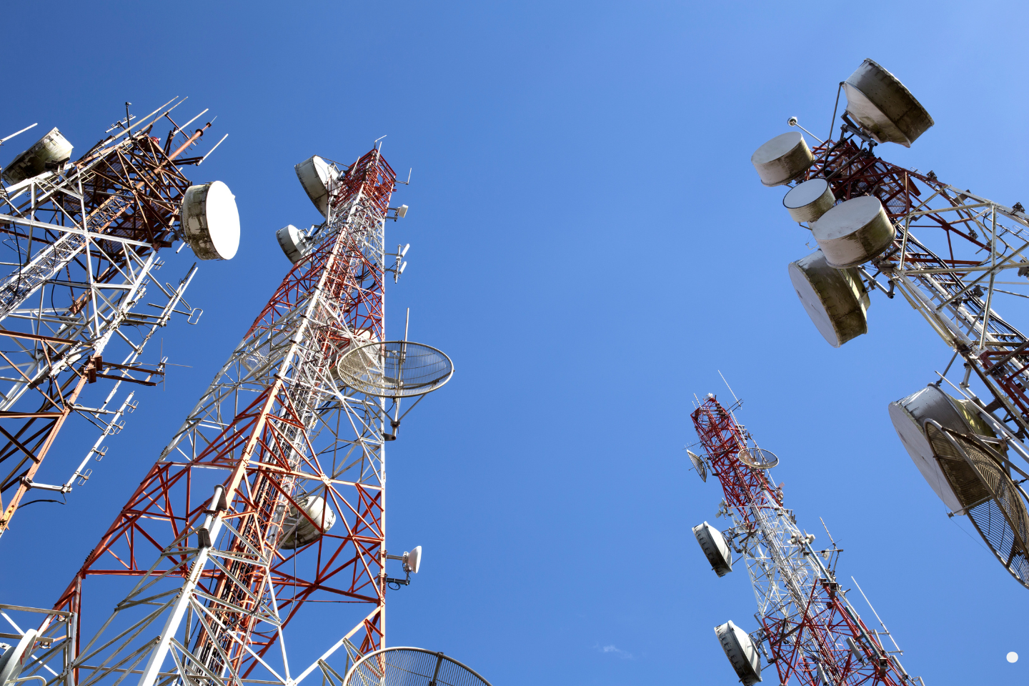 Multiple telecommunications towers rising into a clear blue sky.