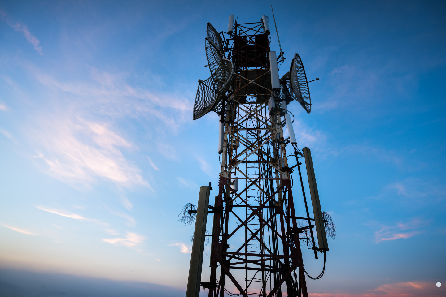 Tall telecommunications tower with antennas against a colorful sky.