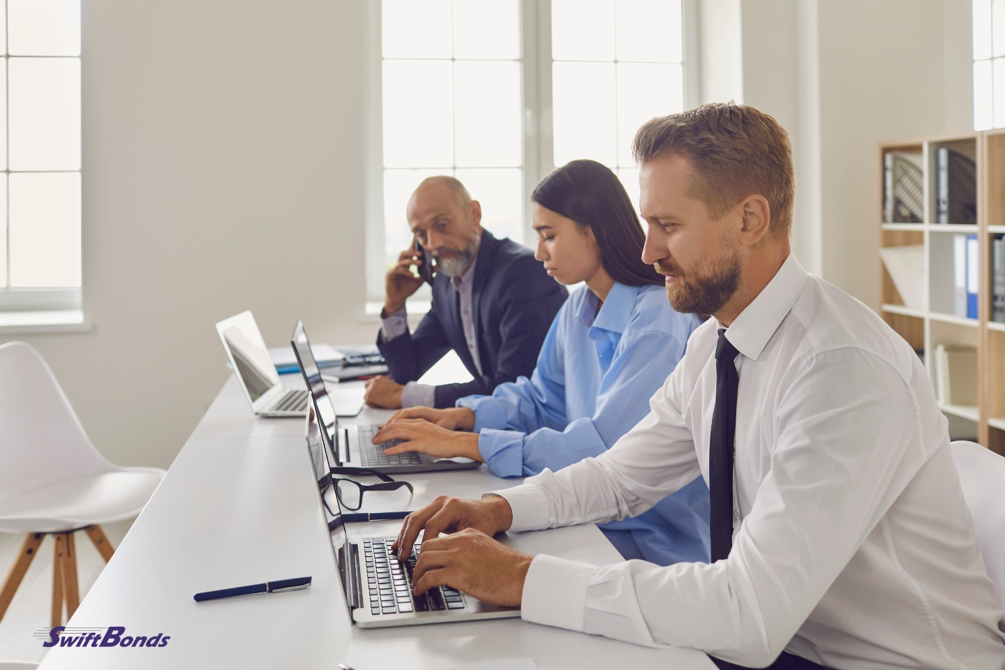 Employees of the company are seated at desks in offices, using laptops, making calls, and collecting debts.