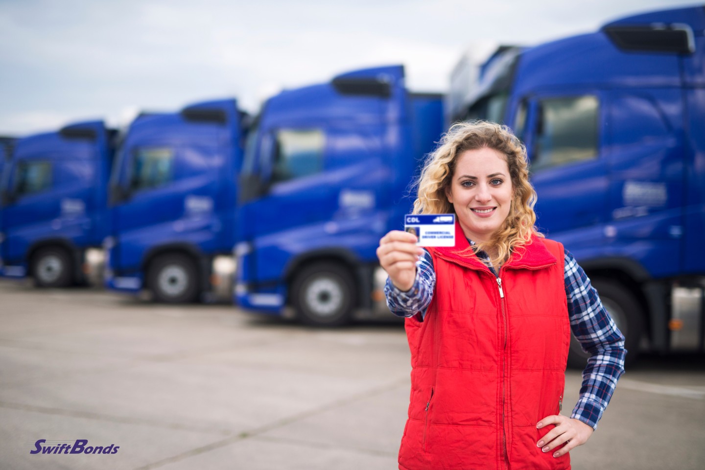 Commercial driving school. In front of truck vehicles, a truck driver displays their driver's license.