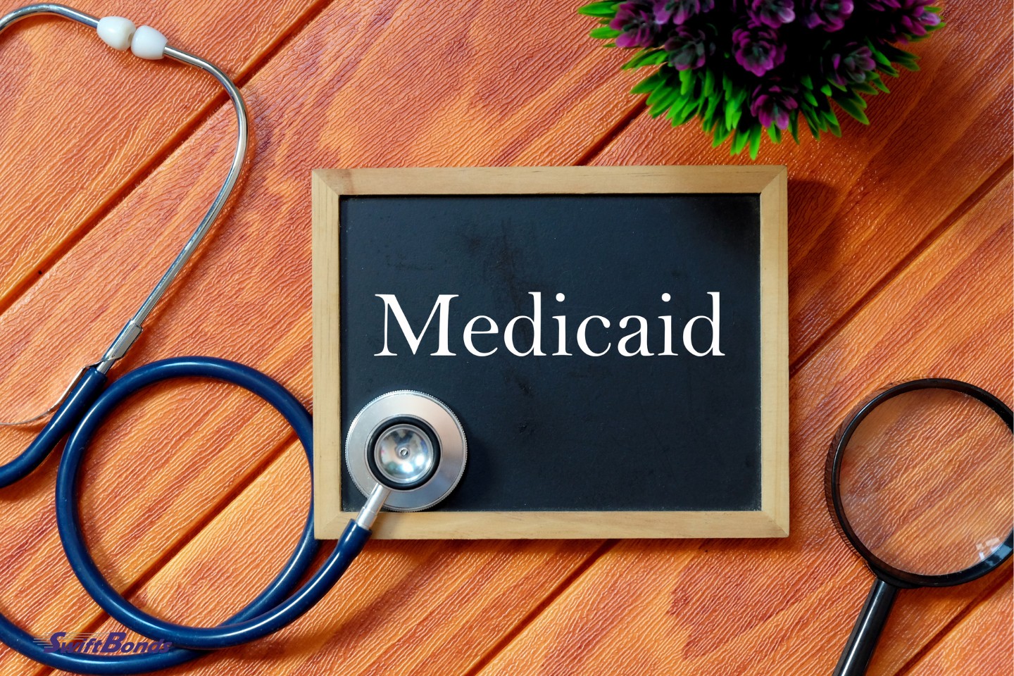 Stethoscope top view. Medicaid is written on a wooden background with a magnifying lens, a plant, and a blackboard.
