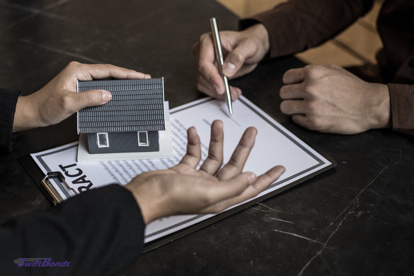 A client and broker sign a contract while holding a miniature model of the house.