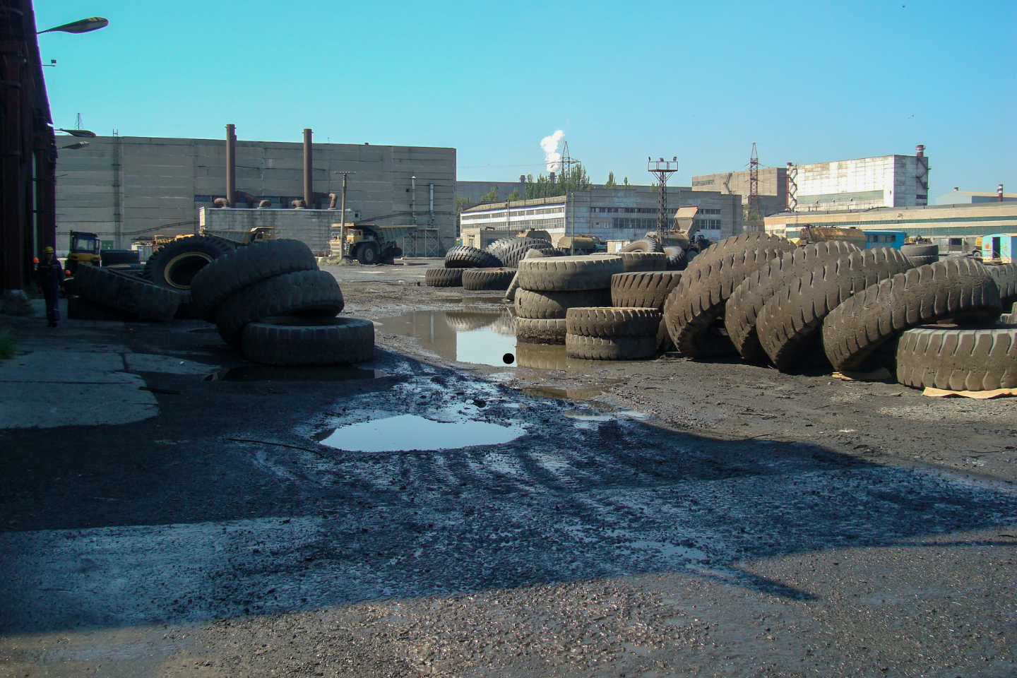 Oversized industrial tires scattered around a muddy lot near old warehouse buildings.