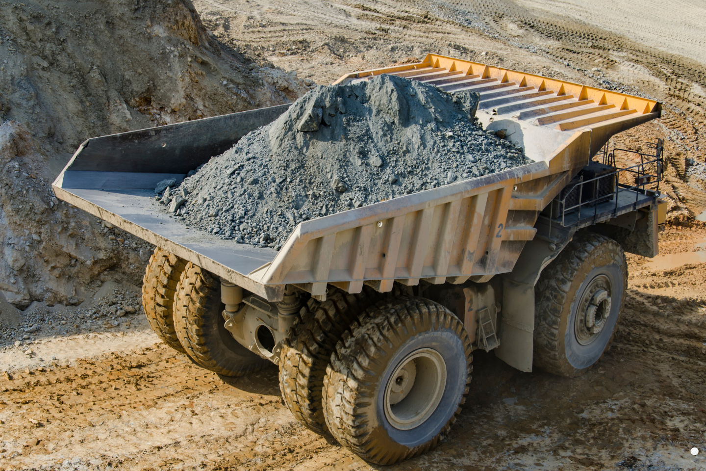 A large mining haul truck loaded with crushed rock driving across a dirt excavation site.