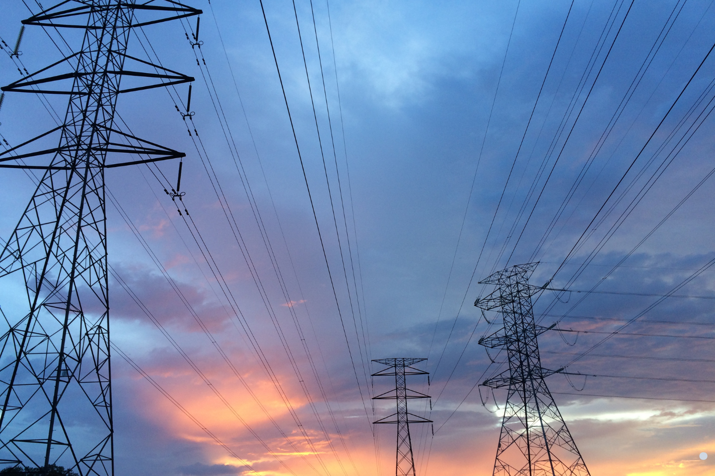 High-voltage power transmission towers and overhead lines stretching across the landscape at sunset.