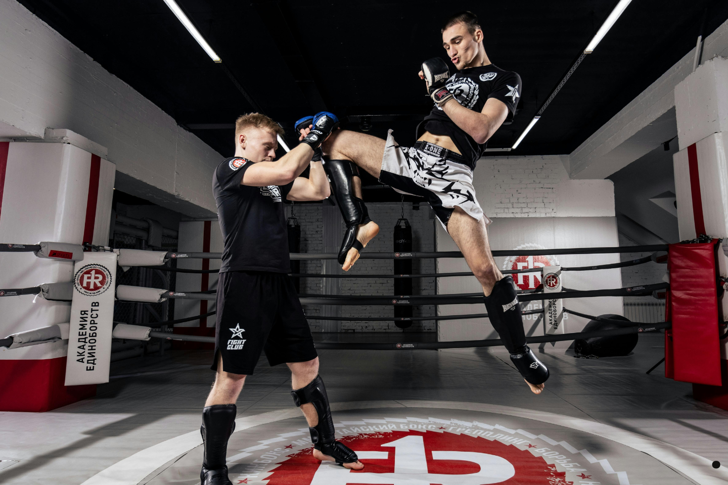 Two MMA fighters sparring in a ring as one delivers a jumping knee strike.
