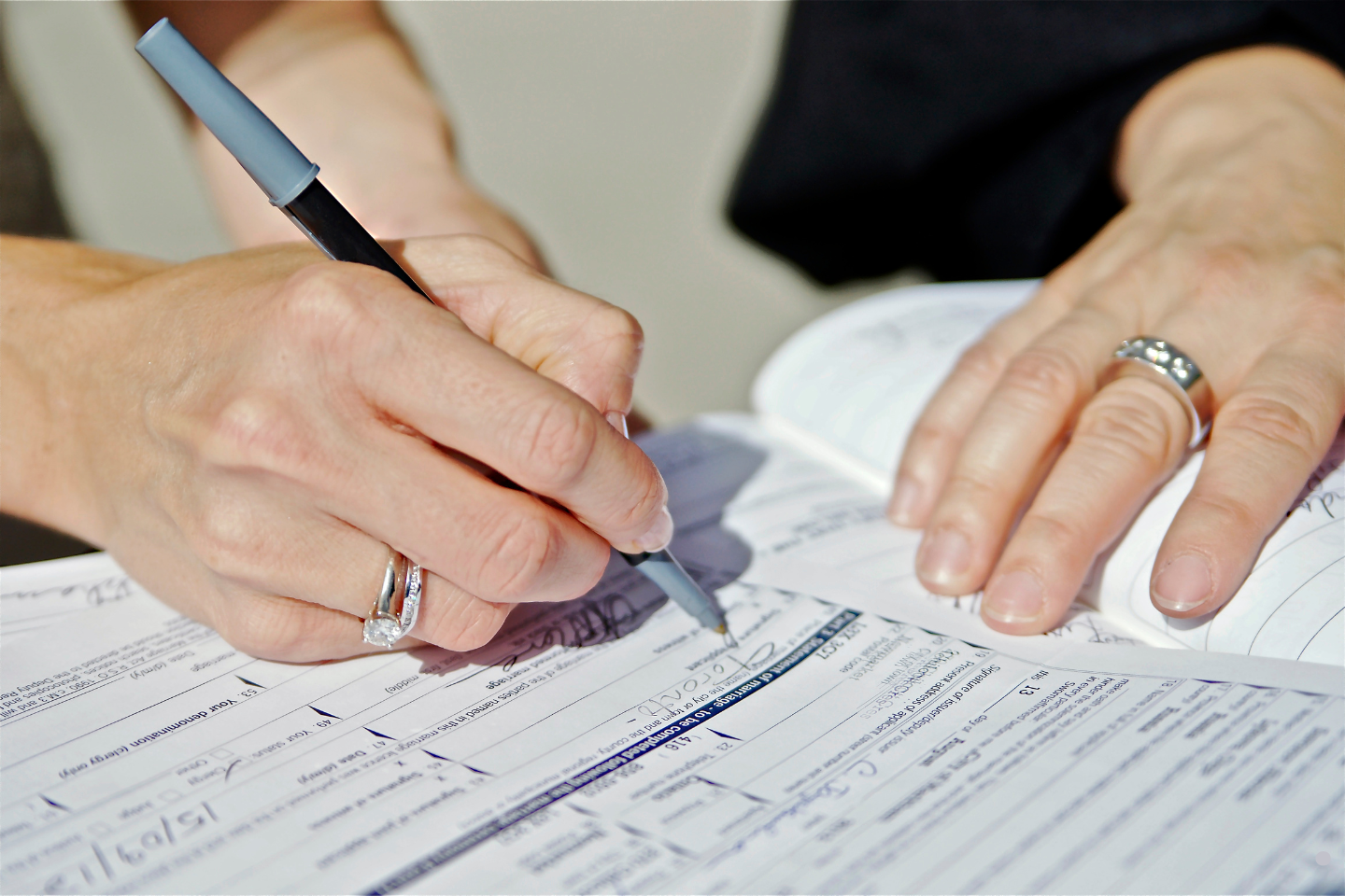 A person filling out and signing registration paperwork with a pen.