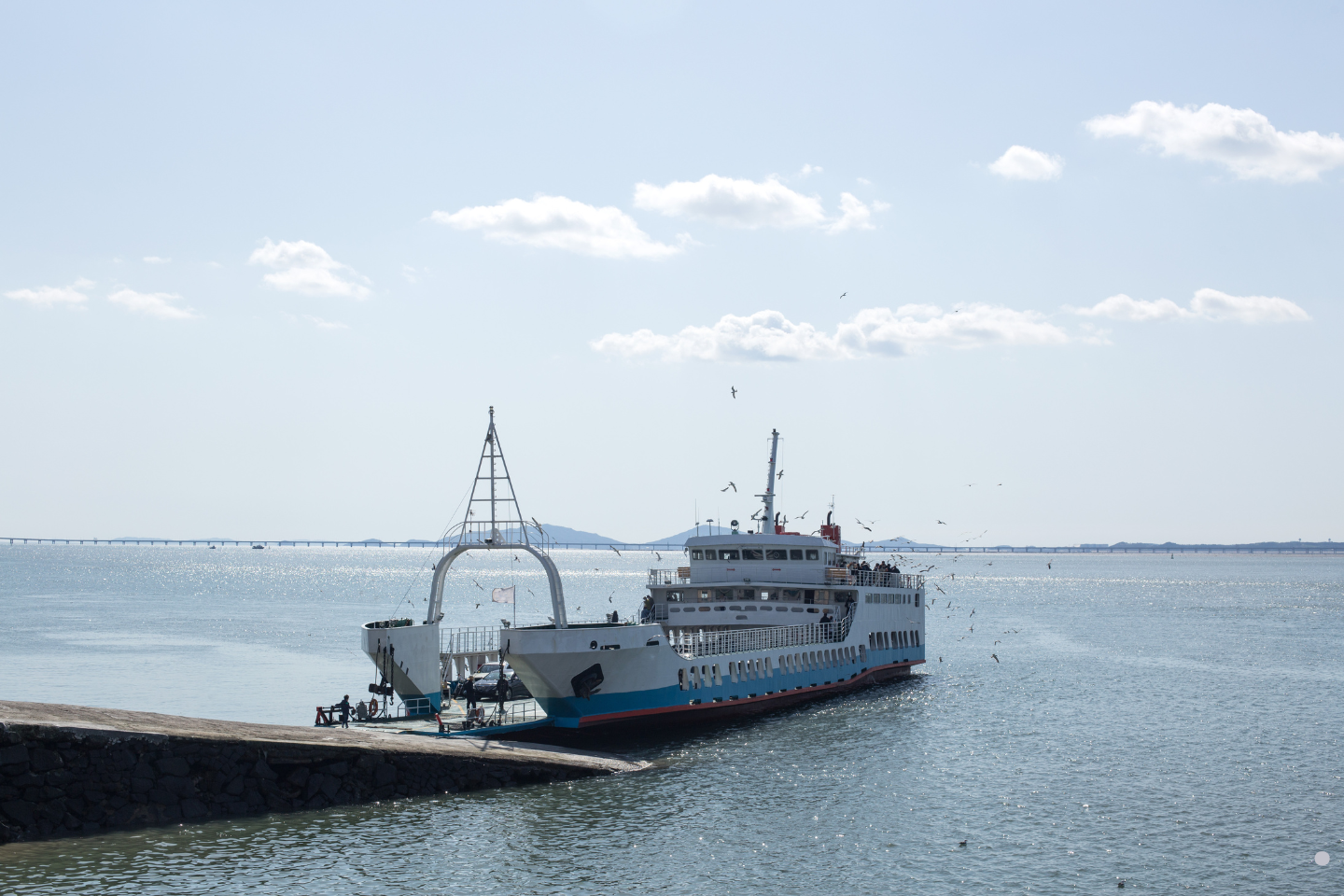 A passenger ferry docked at a pier on a calm, sunny waterfront.