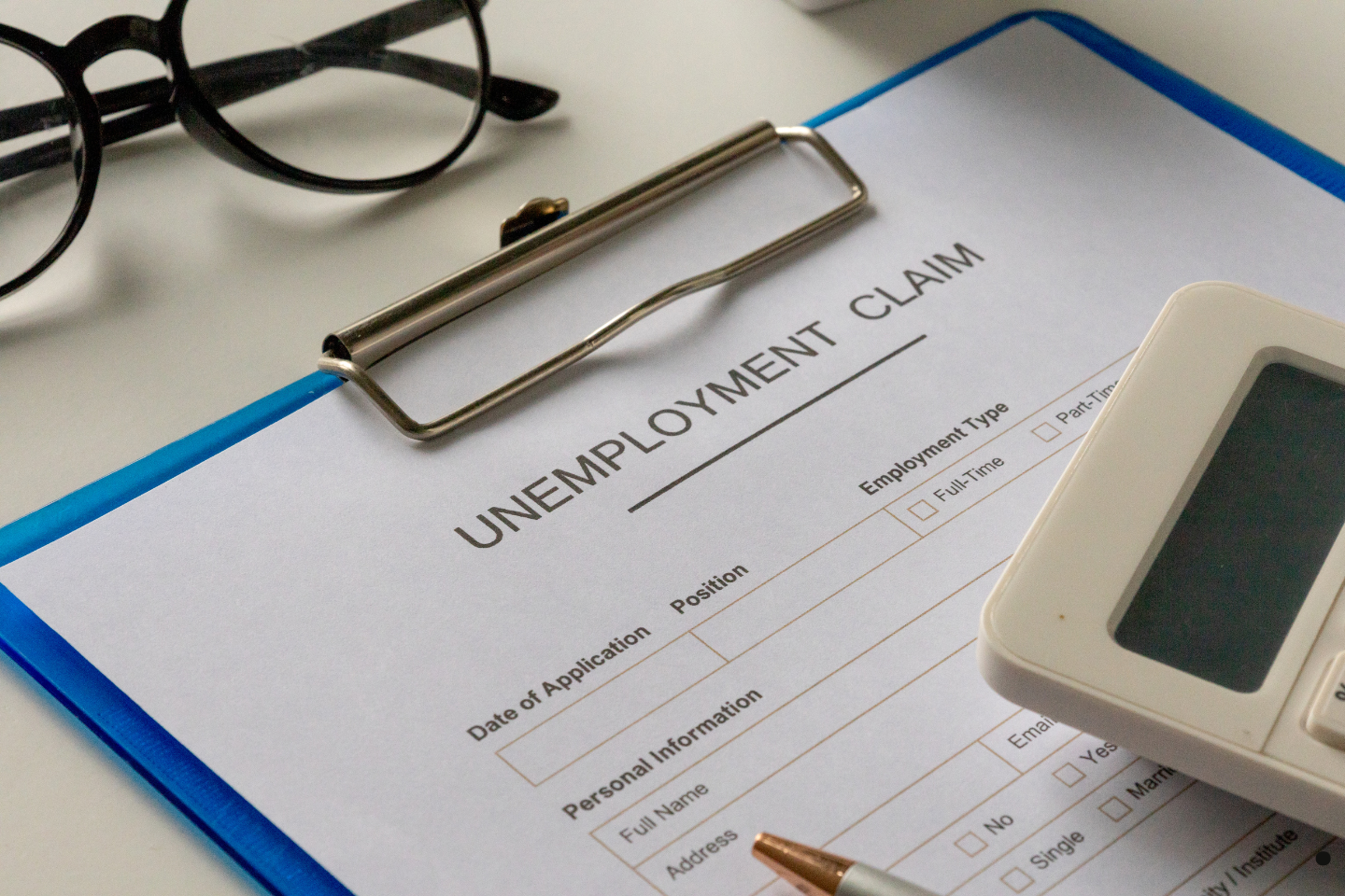Close-up of an unemployment claim form on a clipboard beside glasses and a calculator.