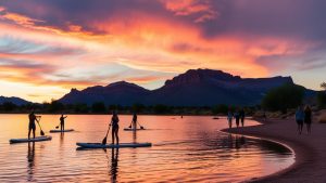 People paddleboarding at sunset on a scenic lake near South Jordan, Utah, with colorful sky and mountain silhouette.