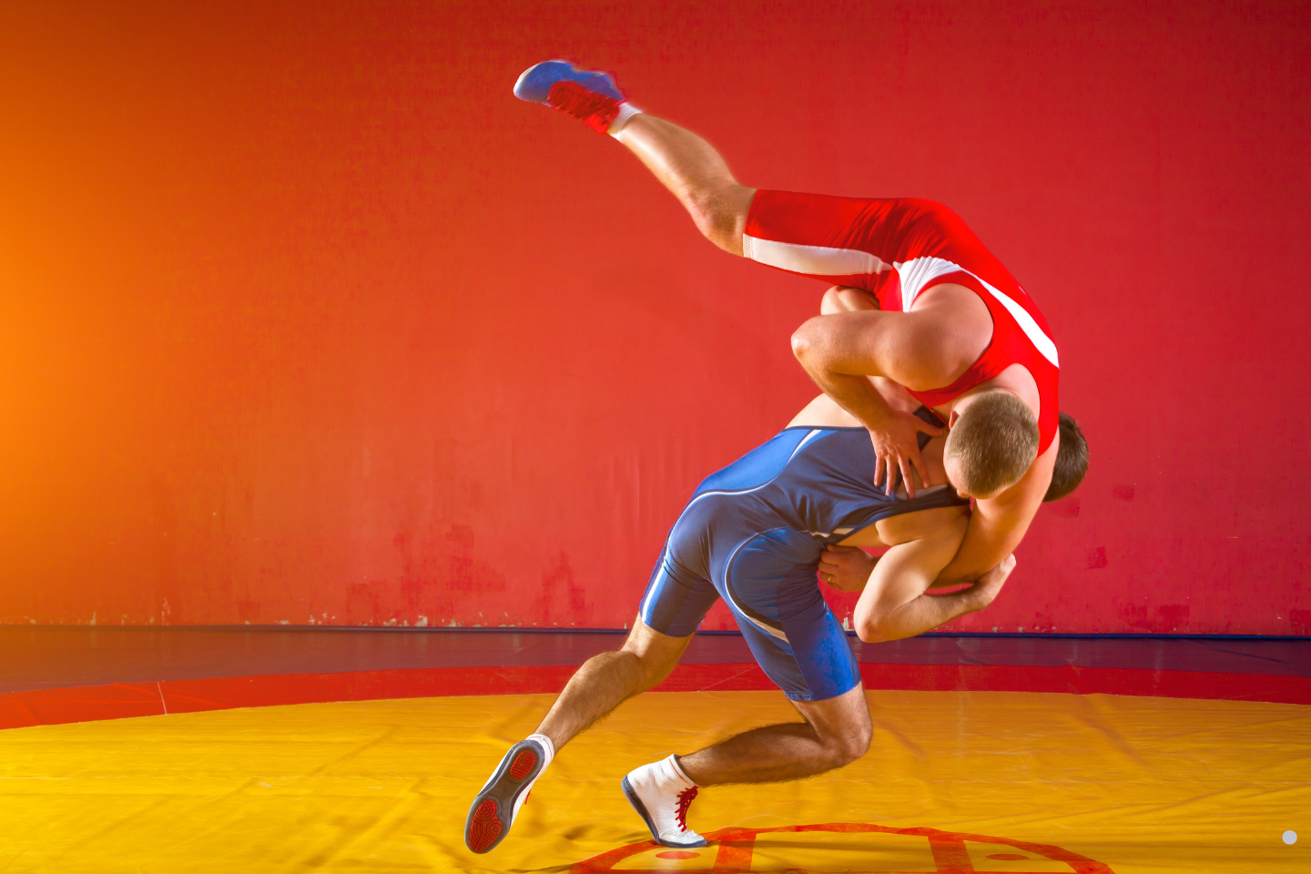 Two wrestlers in singlets performing a high-amplitude throw on a wrestling mat.