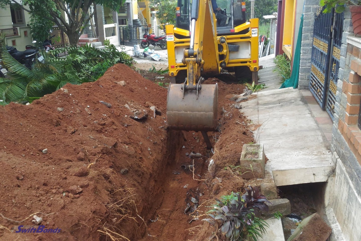 A yellow excavator is digging the road near a house in a residential area.