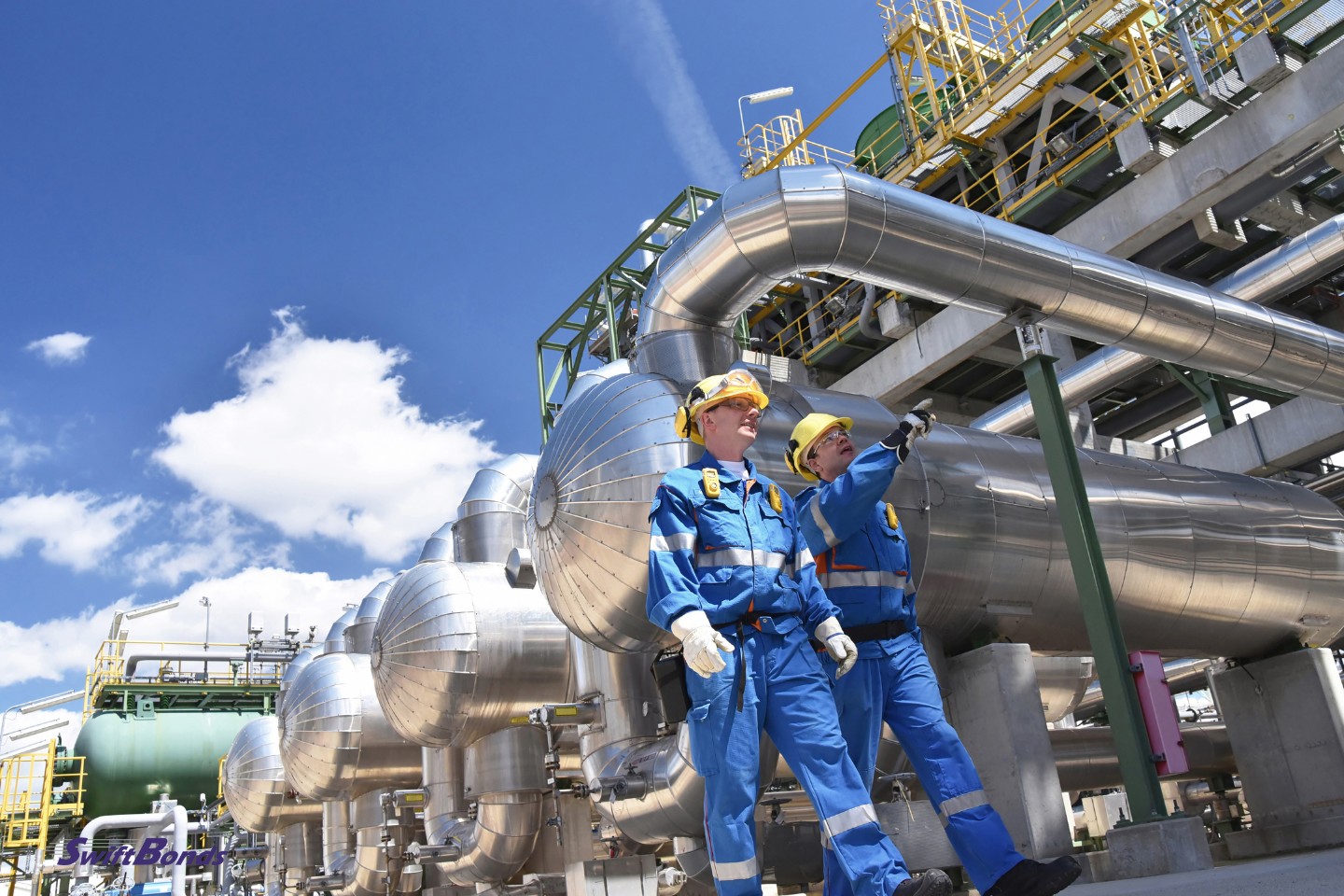 A group of industrial workers using machinery and equipment for oil processing in a refinery.