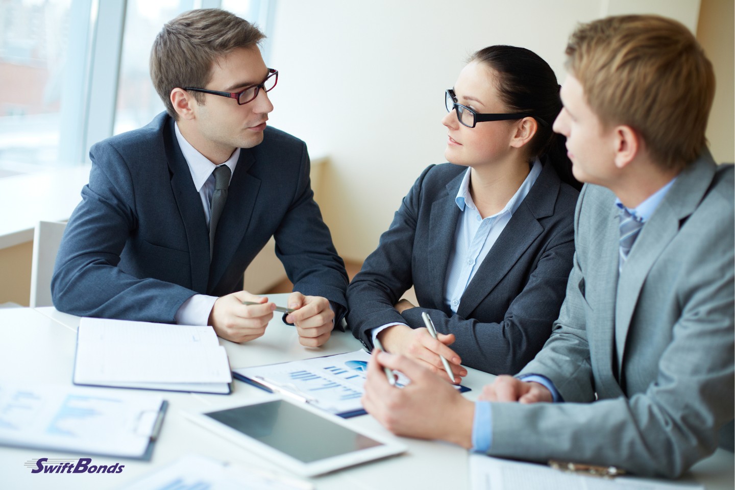 picture of three people negotiating with their paperwork at a table inside the workplace.