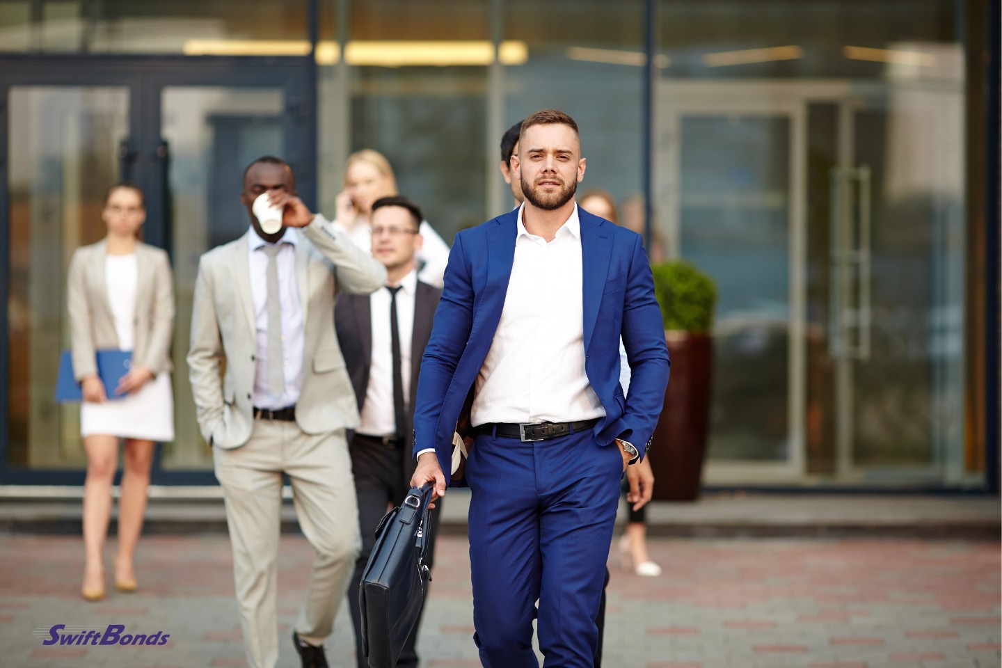 A young employer with a briefcase walks in front of his team.