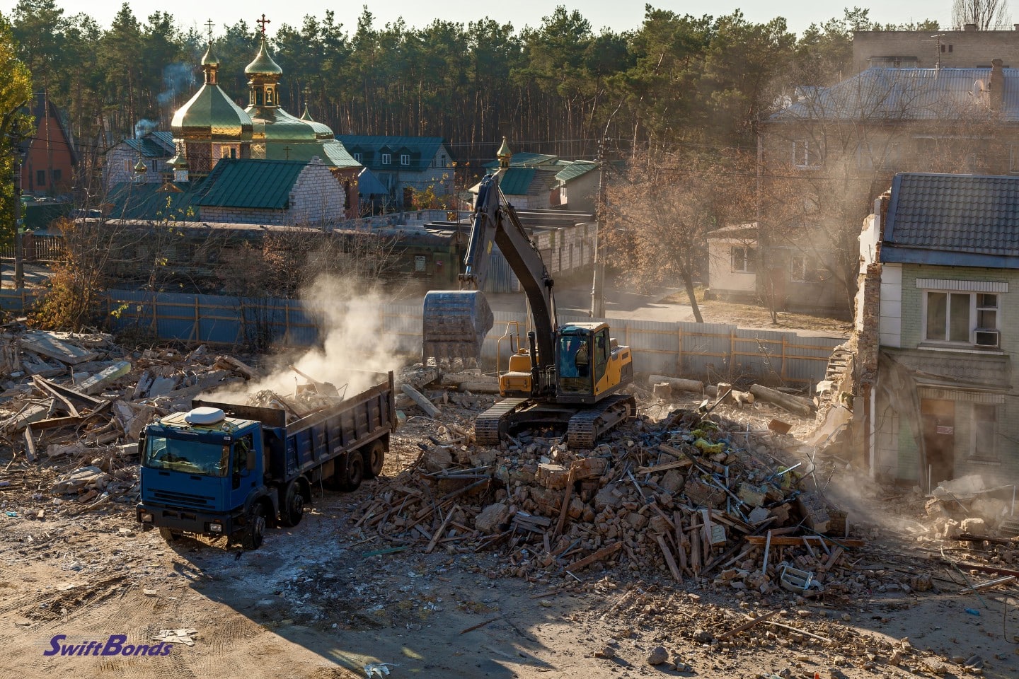 Excavator demolishes the building and loads the remains into a truck.