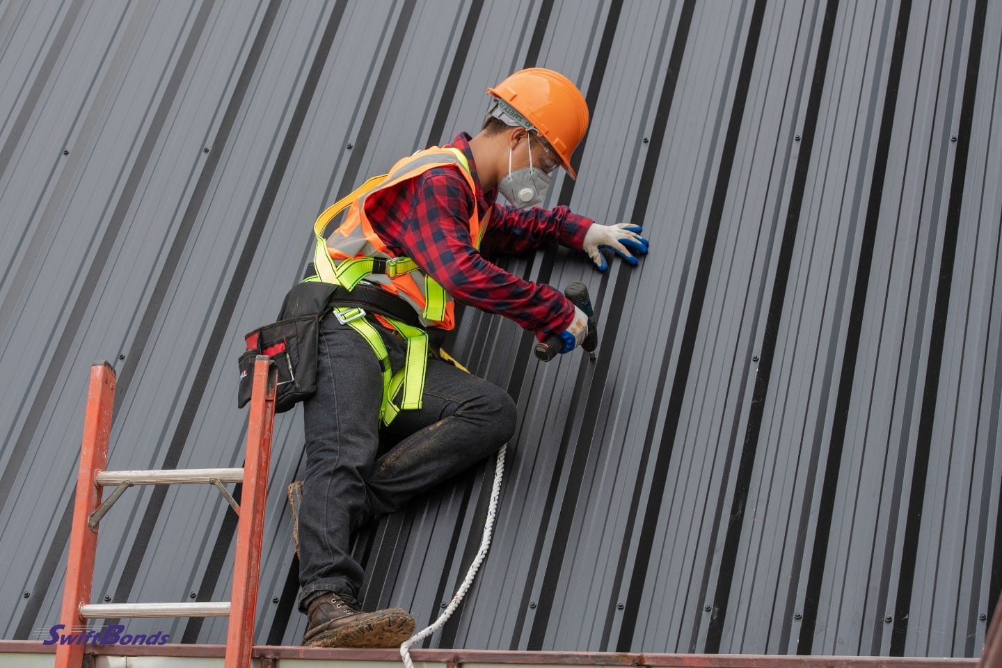 Roofer is installing metal sheets while holding equipment near the ladder.