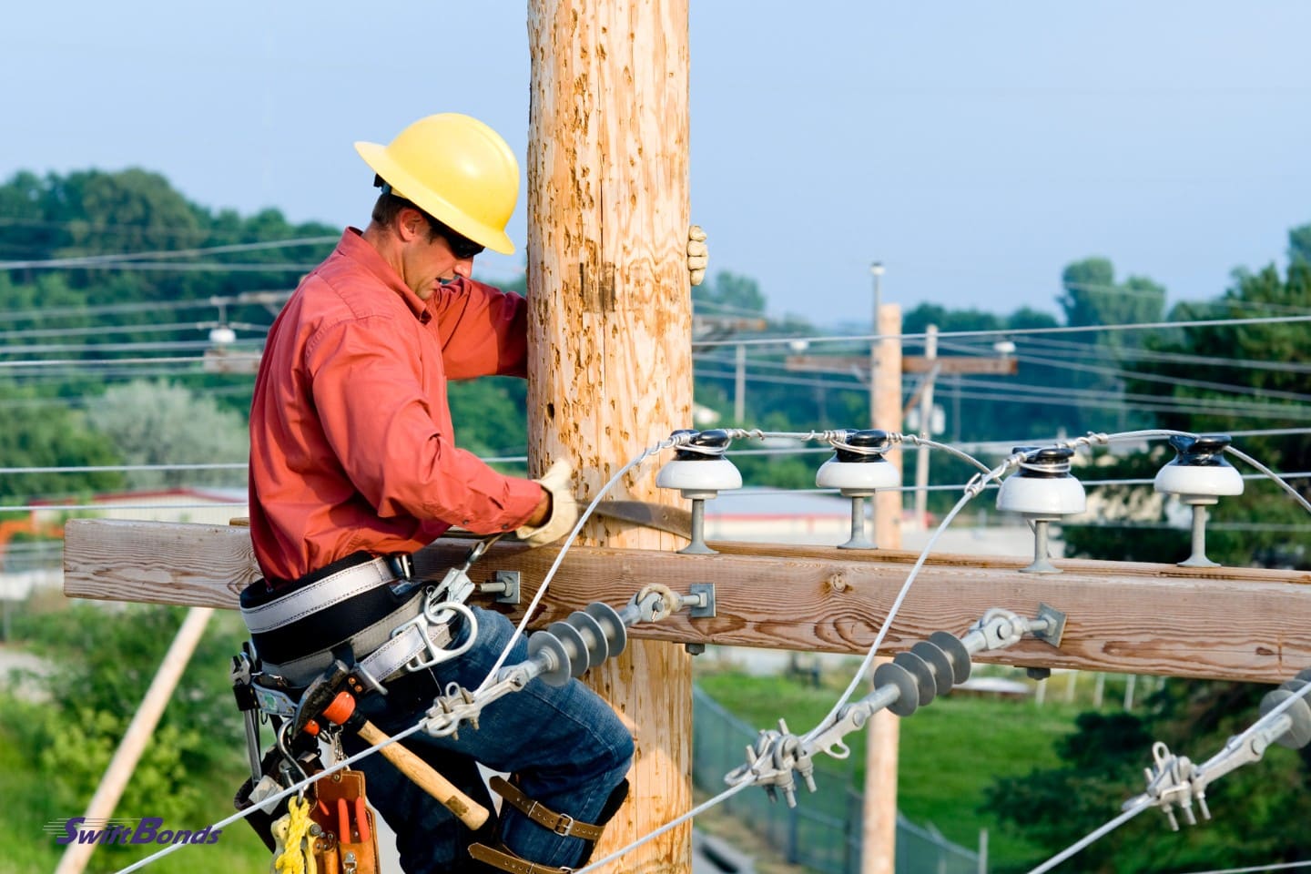 A utility worker is mending electric lines on a pole.