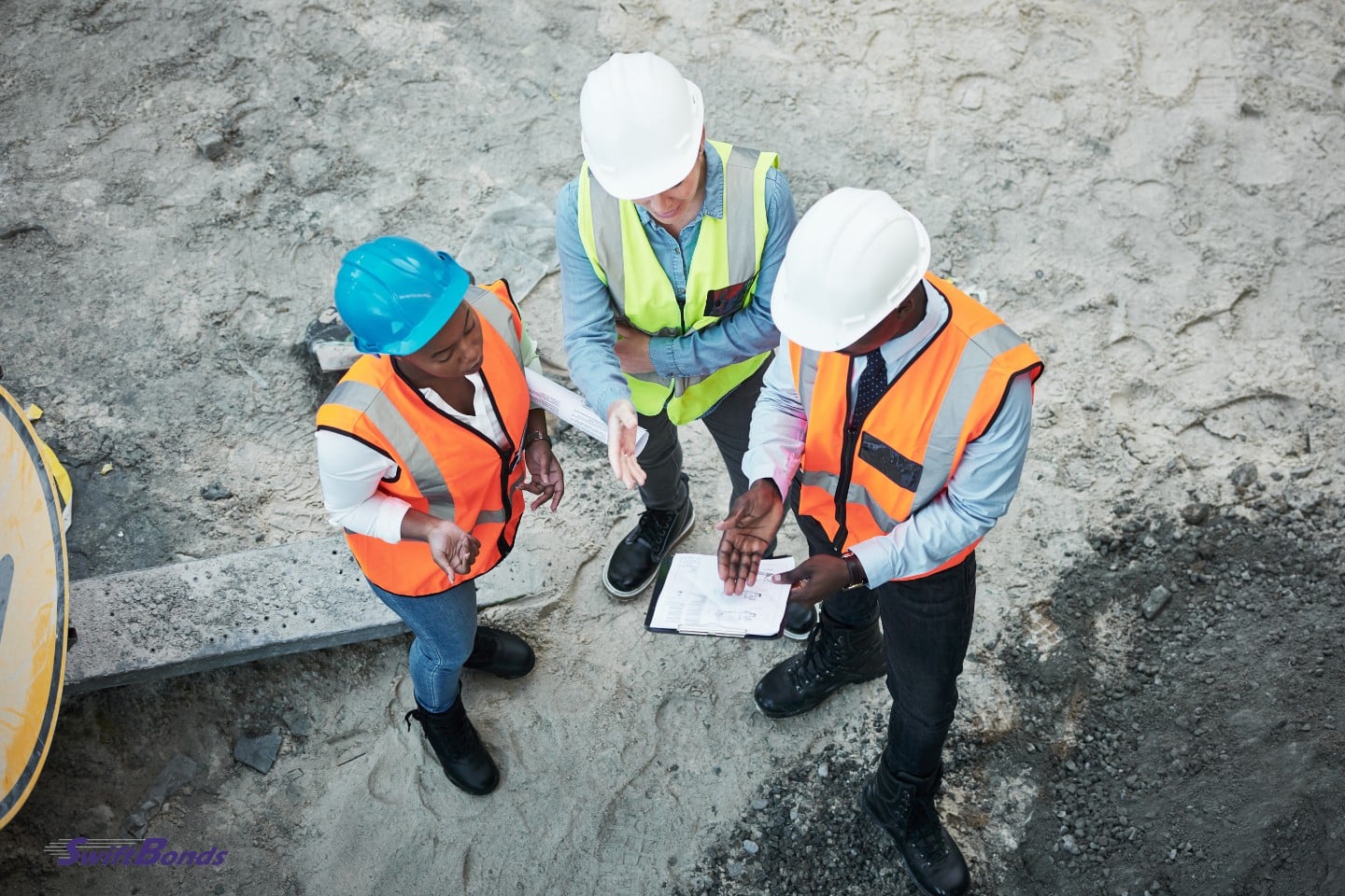 At a construction site, a group of builders review building blueprints.