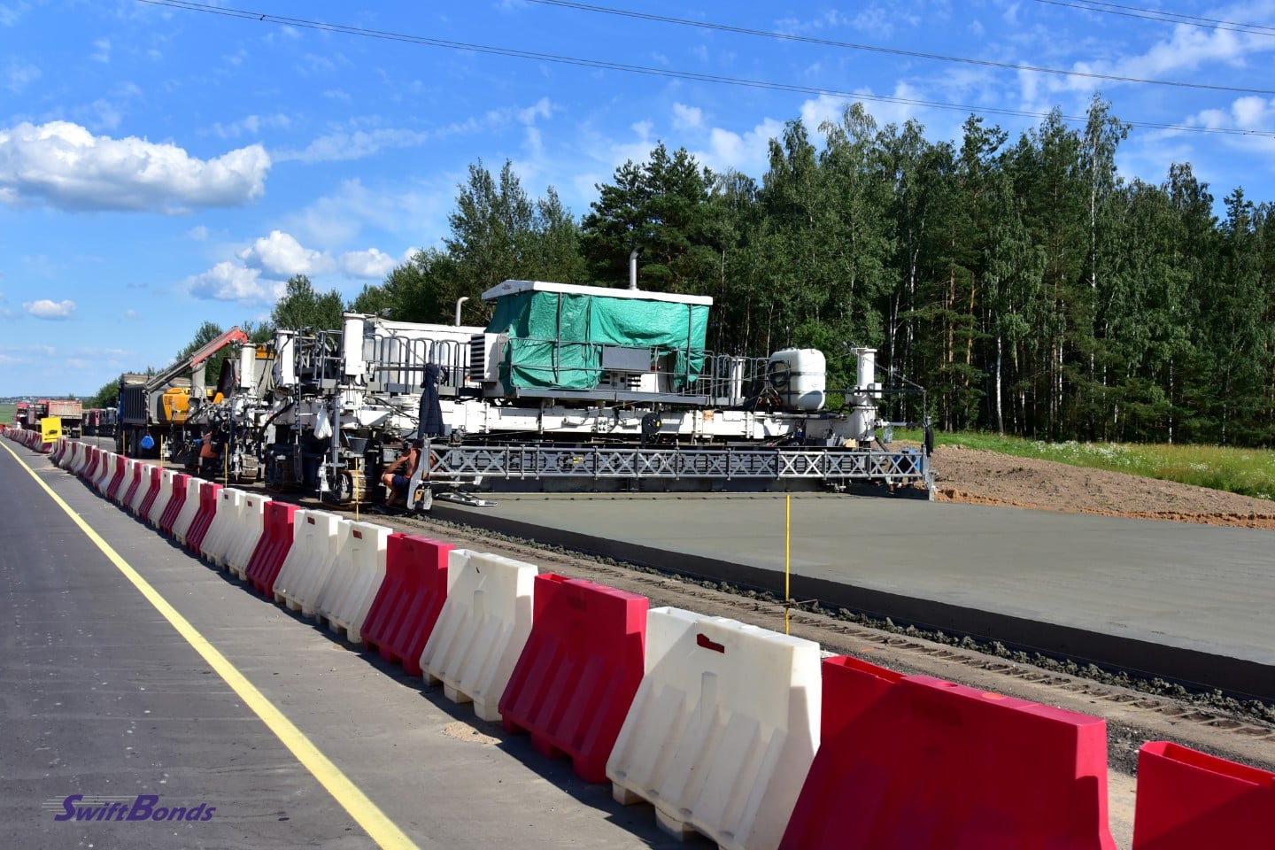 On a construction roadway is a slip-form concrete paver machine.