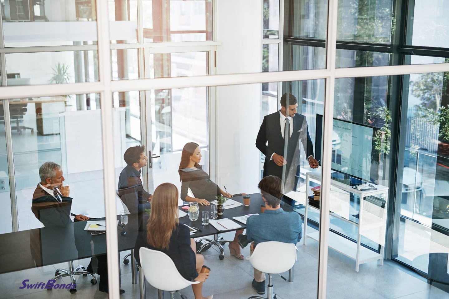 In a glass office, a group of sales reps are gathering.