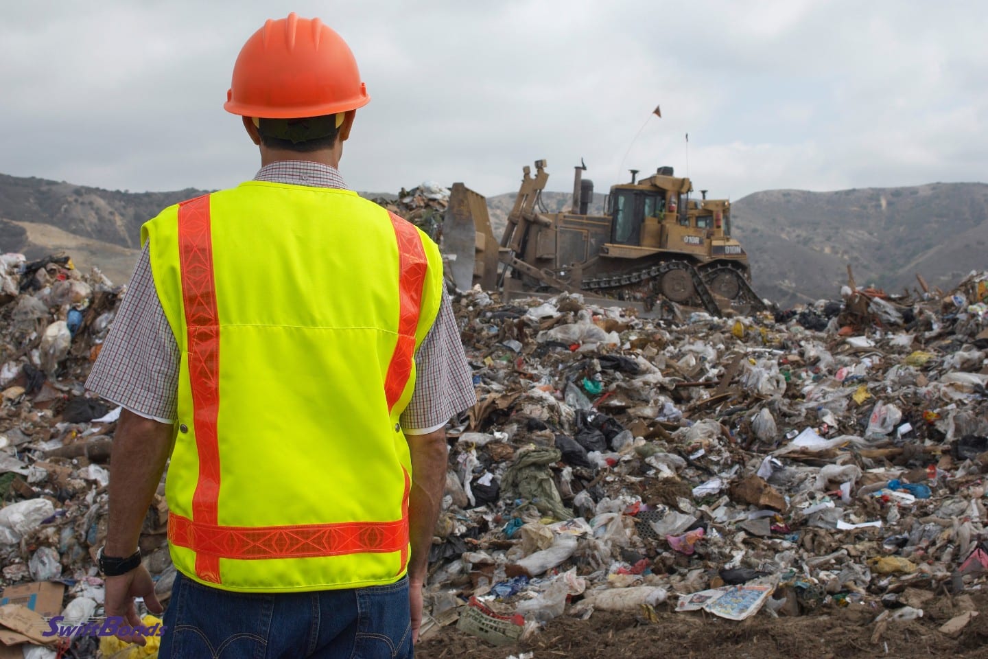 At the landfill, a worker is observing a digger as it moves rubbish.