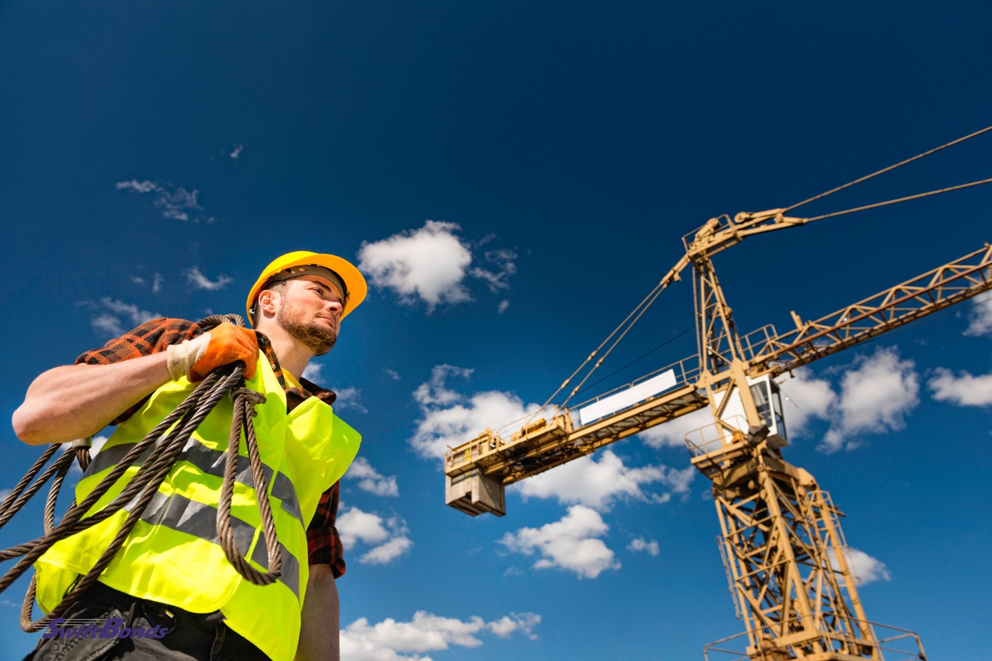 Construction worker carrying cable beneath the tower crane.