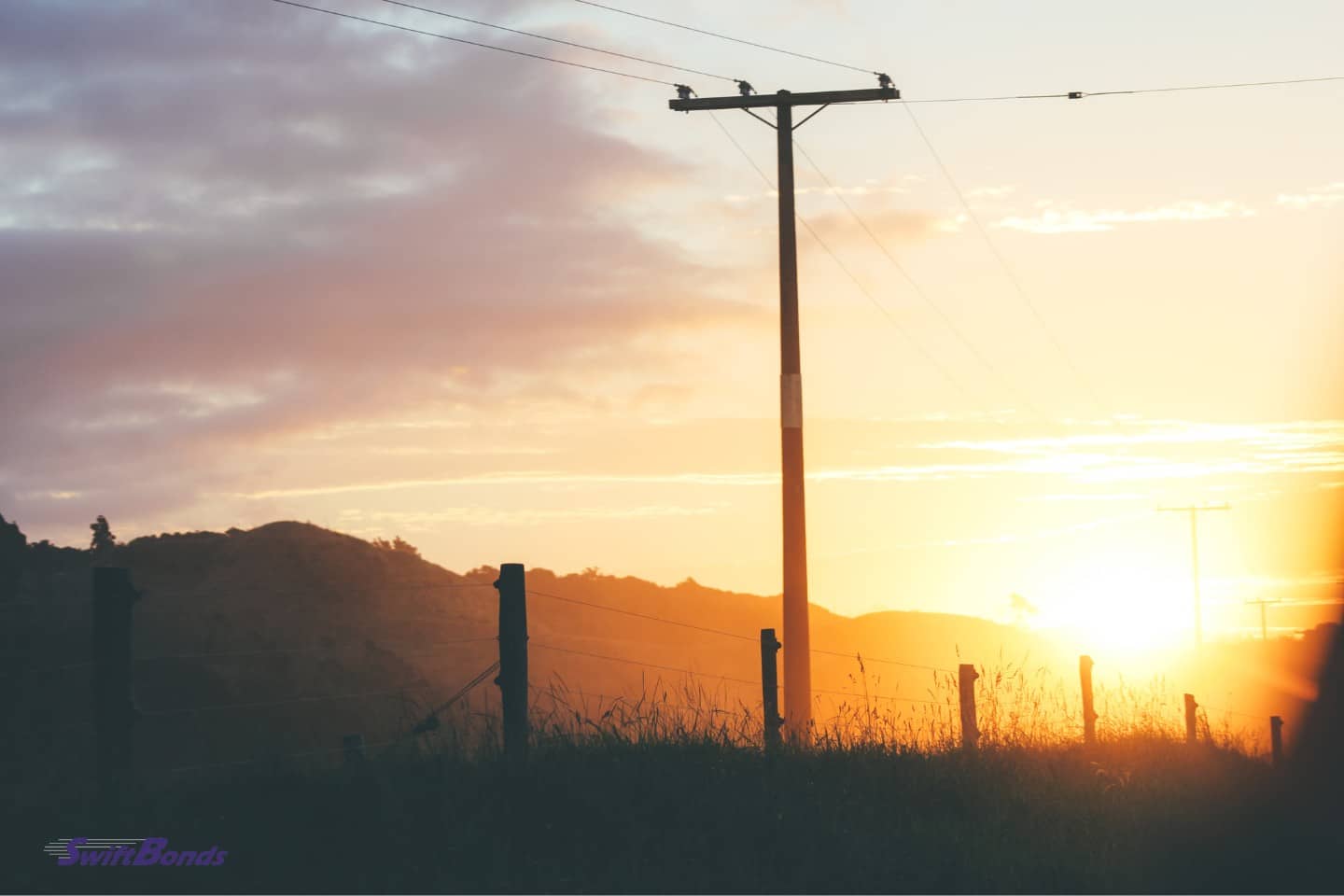 A utility pole at sunset next to a fence.