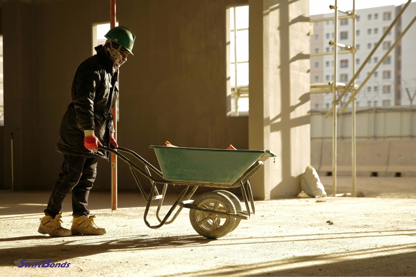 A worker on a building site is pushing a wheelbarrow.