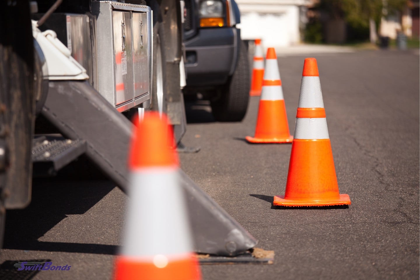 Several orange caution cones and utility truck in street.