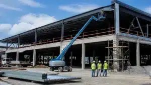 Steel-frame commercial building under construction with contractors and lift equipment