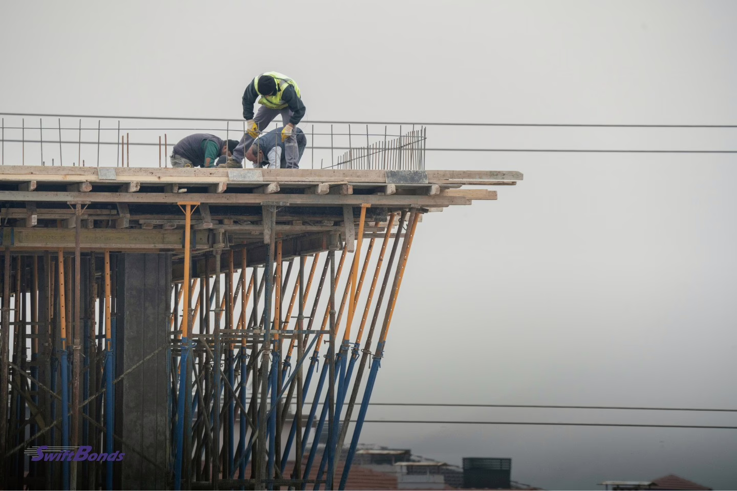 Construction workers operating on a high-rise building in a downtown area, working at height with safety equipment.